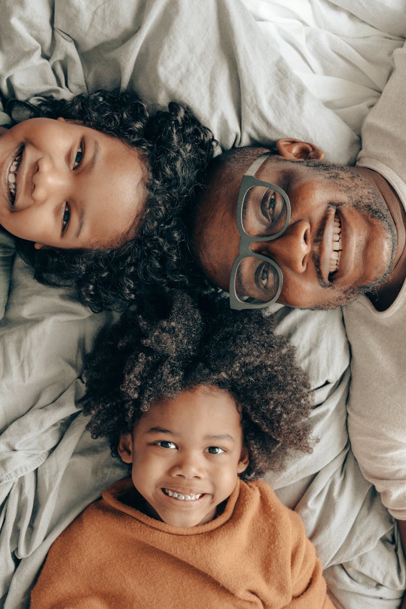 Joyful family of a father with his children enjoying a cozy moment on a bed, smiling warmly.